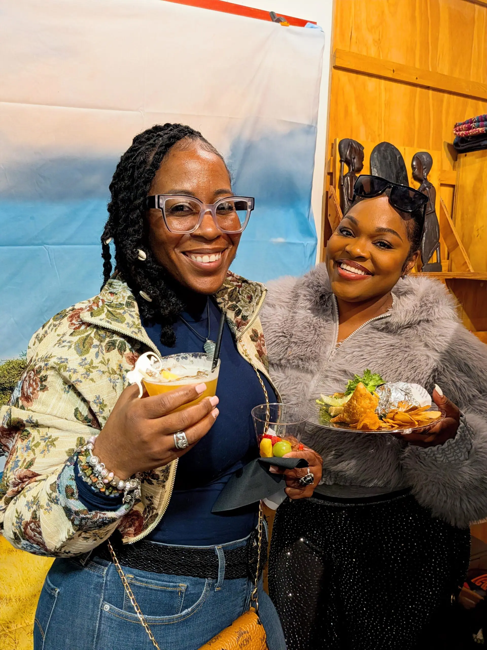 Two women smiling with drinks and food.