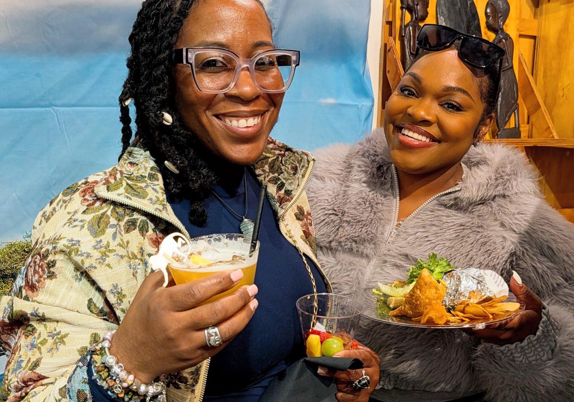 Two women smiling with drinks and food.